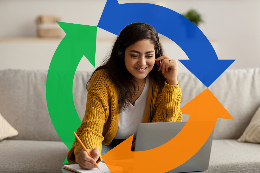 Woman looks at her laptop smiling and writing down something she sees.