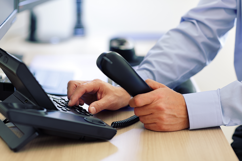 A close up of a man holds a phone and dials numbers with his other hand.