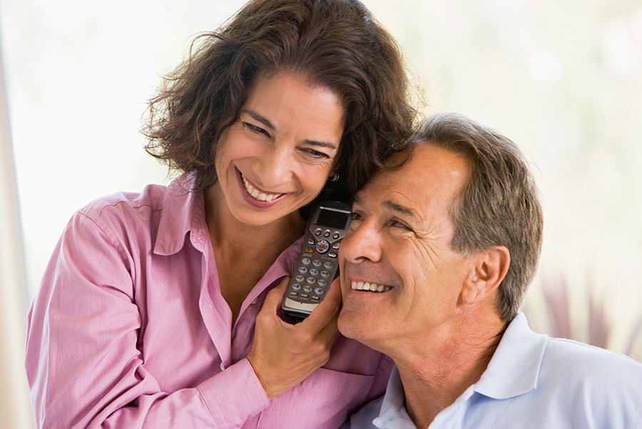 A couple sits closely with heads pressed near to both lsiten to a home phone spear.